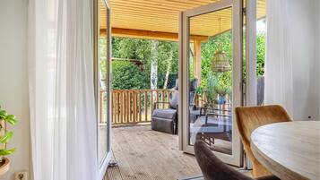 Una porta scorrevole in vetro aperto che dà su una terrazza esterna con tetto in legno, un tavolo, sedie e un lampadario.