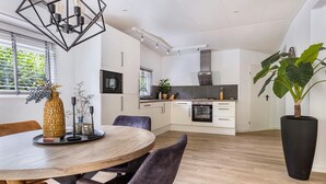 A modern kitchen with white cabinets, a built-in oven, and a dining area with a wooden table and chairs. - 1 bedroom stunning home in Erm (Erm)