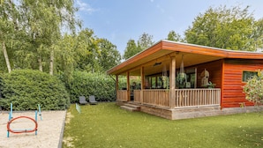 A wooden cabin with a porch, surrounded by a well-maintained lawn and dense trees. - 1 bedroom stunning home in Erm (Erm)