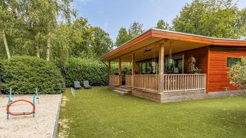 Una baita di legno con un portico, circondata da un prato curato e alberi fitti.