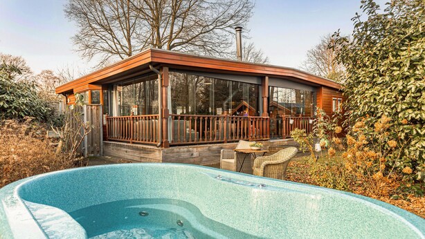 A wooden cabin with a glass enclosure, a hot tub, and a deck with wicker furniture. - 2 bedroom pet friendly home in Erm (Erm)