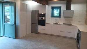 Eine moderne Küche mit weißen Schränken, einem Edelstahl-Kühlschrank, einem eingebauten Backofen, einer Mikrowelle, einem Fenster mit Blick und einer Waschmaschine.