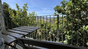 Eine Terrasse mit Metallgeländer, Holzbanken und Blick auf eine Landschaft mit Bäumen und Hügeln in der Ferne.