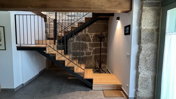 Eine Treppe mit Holzstufen und schwarzen Geländern, die zu einer Empfangshalle mit Kleiderhaken und einem Bilderrahmen führt.