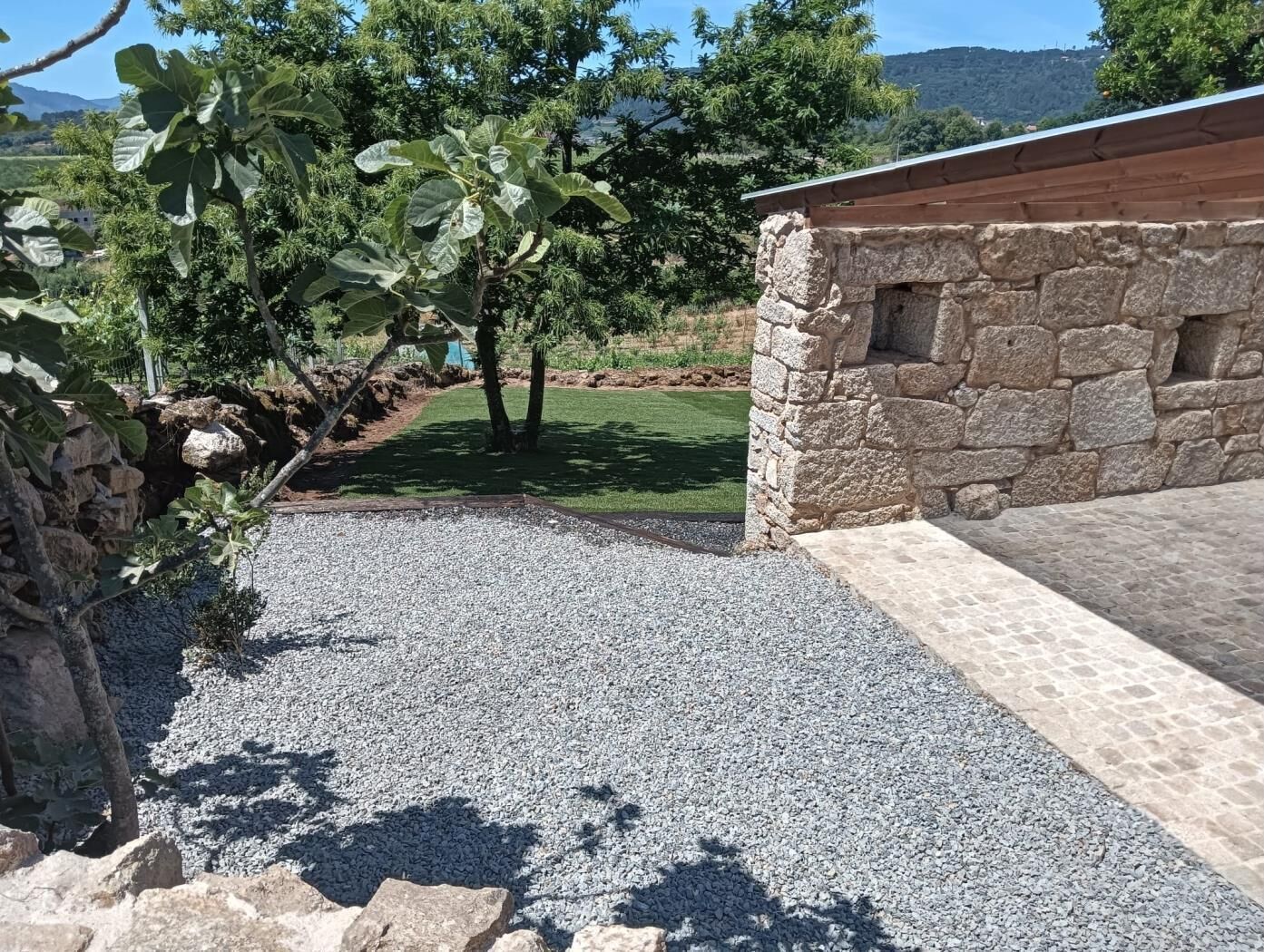 A stone building with a gravel driveway leading to a grassy area with trees.