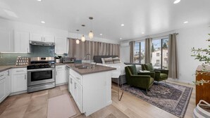 Une cuisine moderne avec un îlot central, un coin repas avec un canapé et une chambre dotée d’une grande fenêtre.