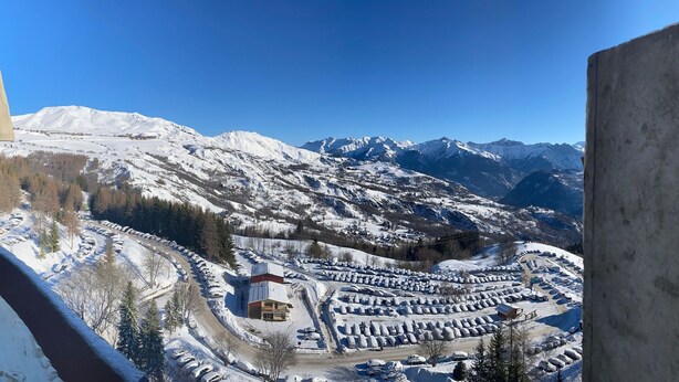 Een bergachtig landschap bedekt met sneeuw, met een parkeerplaats en gebouwen op de voorgrond.