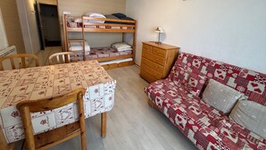 Een kleine kamer met stapelbedden, een slaapbank, een tafel en een dressoir.