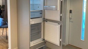 Une cuisine moderne dotée d’un réfrigérateur encastré, d’un coin repas avec une chaise et d’une vue sur l’extérieur grâce à une fenêtre.