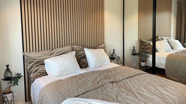 Une chambre moderne avec un grand lit, un miroir et un mur recouvert de lattes de bois.