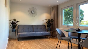 Un salon moderne avec un canapé gris, une table ronde et deux plantes en pot.