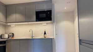 Une cuisine compacte avec des meubles gris, un four à micro-ondes encastré, une machine à café et un verre à vin posé sur le comptoir.