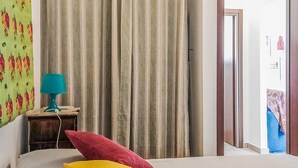 Una habitación de hotel con cama, mesita de noche y una lámpara, y una cortina.
