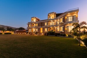 A multi-story building with a flat roof, multiple balconies, and a well-lit entrance. - Suryagarh Club And Resort (Udaipur)