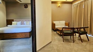 Una habitación de hotel moderna con una cama grande, una zona de estar con sofá y sillones, y un ventilador de techo.