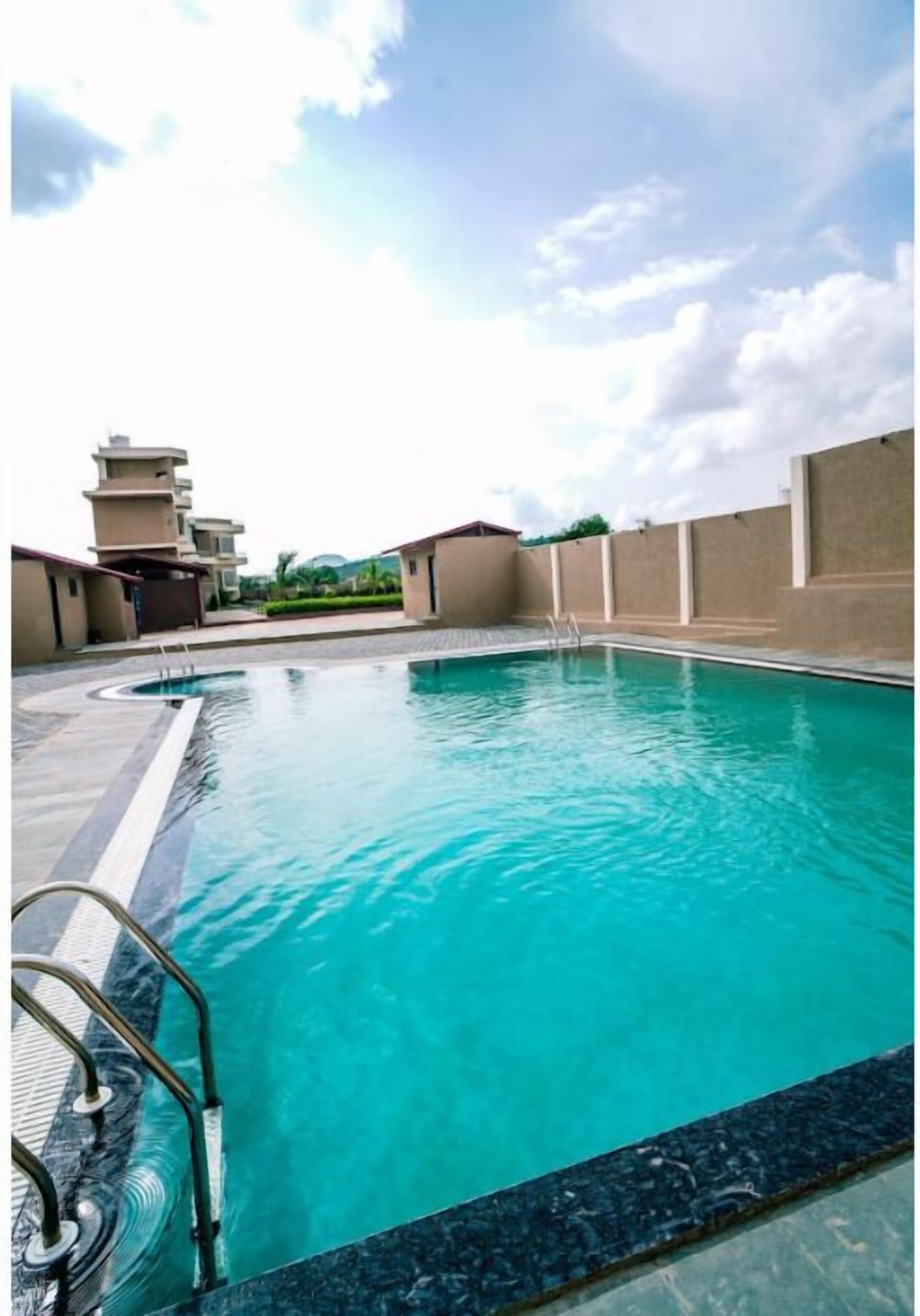 A swimming pool with clear blue water, surrounded by a tiled deck and a low wall.