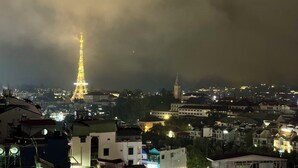 En nattbild av en stadsbild med ett framträdande, upplyst torn som liknar Eiffeltornet, omgivet av olika byggnader och en molnig himmel.