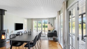 A modern living room with a fireplace, a dining table with chairs, a sofa, and a TV mounted on the wall.