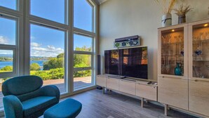Una sala de estar moderna con ventanas amplias, un televisor de pantalla plana, un mueble con cristalería y vistas a un lago.