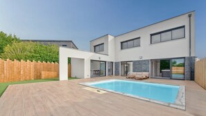 Une maison moderne à deux étages, dotée d’une piscine, d’un espace de détente extérieur et d’une clôture en bois.