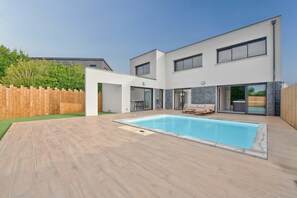 A modern two-story house with a swimming pool, outdoor seating, and a wooden fence.
