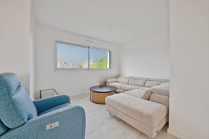 A modern living room with a blue armchair, beige sofa, and a round wooden coffee table.