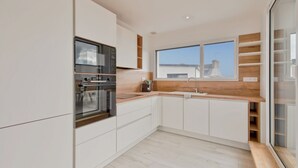 Une cuisine moderne avec des meubles blancs, un four encastré et une grande fenêtre donnant sur le paysage urbain.