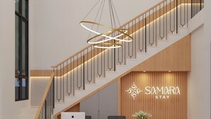 A modern reception area with a marble reception desk, a wooden reception desk, a grey sofa, and a staircase with a wooden railing. - Samara Stay by Sinergi (Semarang)
