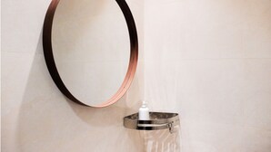 A bathroom with a large oval mirror mounted on the wall, a small sink with a soap dispenser, and a metallic tray. - Samara Stay by Sinergi (Semarang)