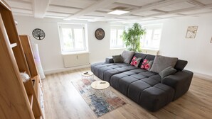 A modern living room with a dark grey sectional sofa, a round coffee table, and a large potted plant. - Apartment 'Alexandra' with Shared Terrace, Shared Garden and Wi-Fi (Aldingen)