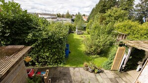 A residential backyard with a lawn, potted plants, a wooden shed, and a corrugated metal fence. - Apartment 'Alexandra' with Shared Terrace, Shared Garden and Wi-Fi (Aldingen)