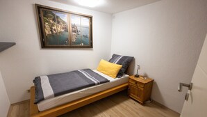 A single bed with a wooden frame, a small bedside table, and a nightstand. A window with a coastal view is above the bed. - Apartment 'Alexandra' with Shared Terrace, Shared Garden and Wi-Fi (Aldingen)