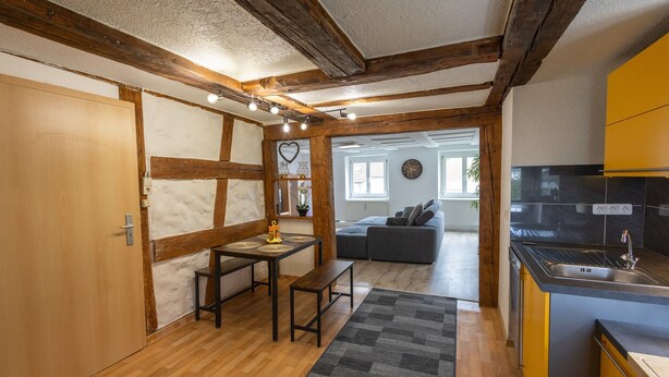 A compact kitchen with wooden beams, a dining area with a bench, and a sofa in the background. - Apartment 'Alexandra' with Shared Terrace, Shared Garden and Wi-Fi (Aldingen)