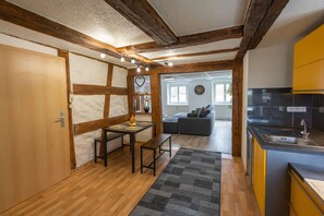 A compact kitchen with wooden beams, a dining area with a bench, and a sofa in the background.