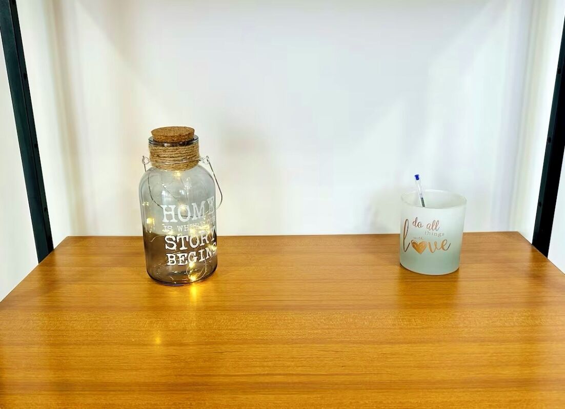 A clear glass bottle with text and a white candle with a blue candle holder on a wooden table.
