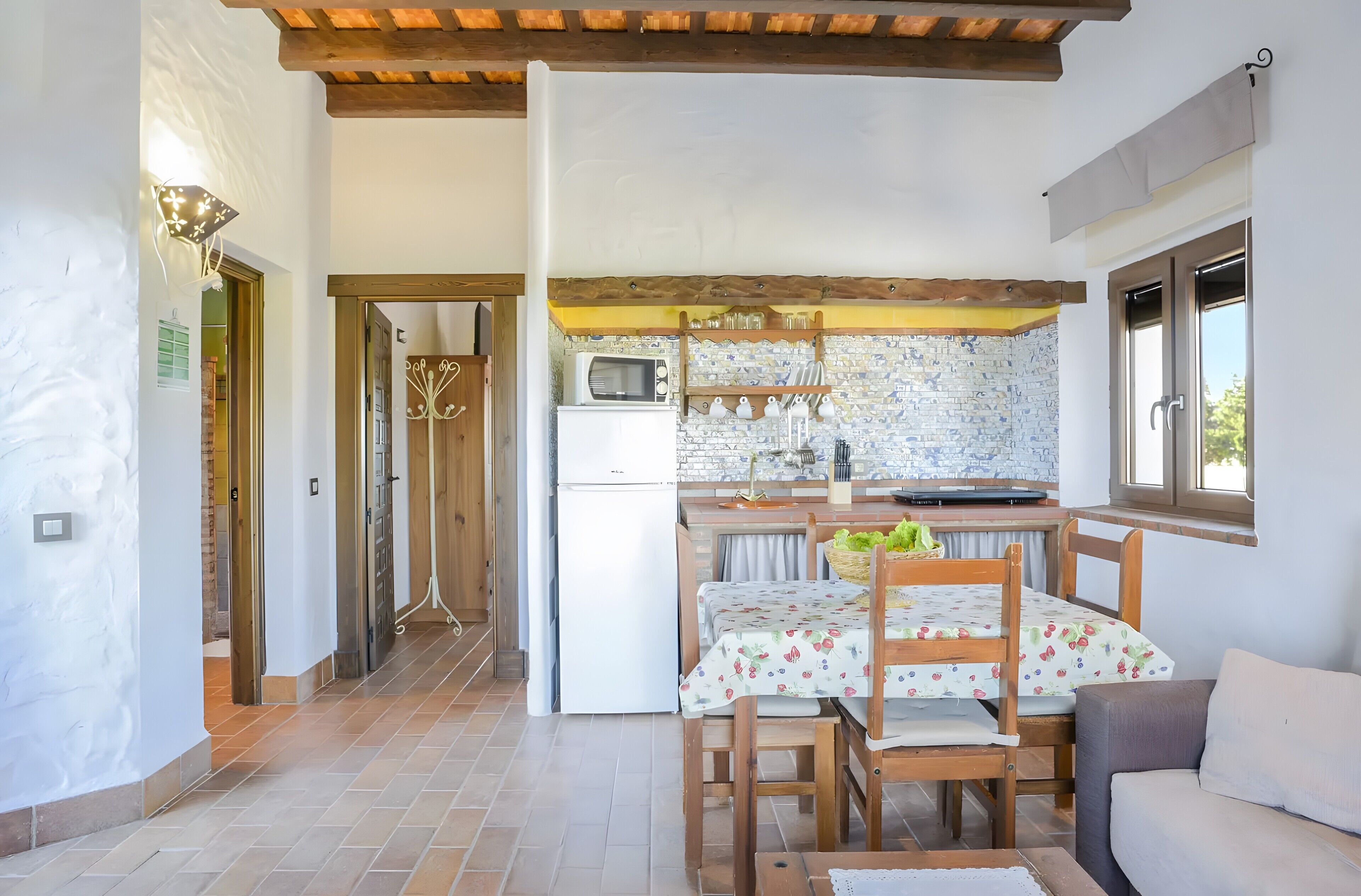 Cocina compacta con microondas, refrigerador y comedor con mesa y sillas.