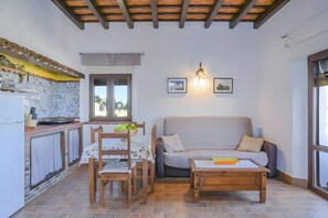 A cozy living area with a sofa, coffee table, and dining table, a kitchen with a tiled backsplash, and a window with curtains.