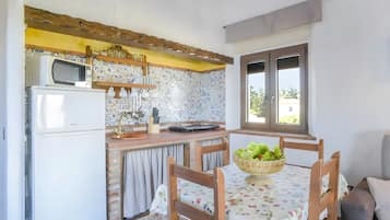 Una cocina con microondas, refrigerador y un salpicadero de ladrillo. Hay una mesa de comedor con sillas y una cesta de fruta.