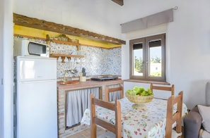 Una cocina con microondas, refrigerador y un salpicadero de ladrillo. Hay una mesa de comedor con sillas y una cesta de fruta.