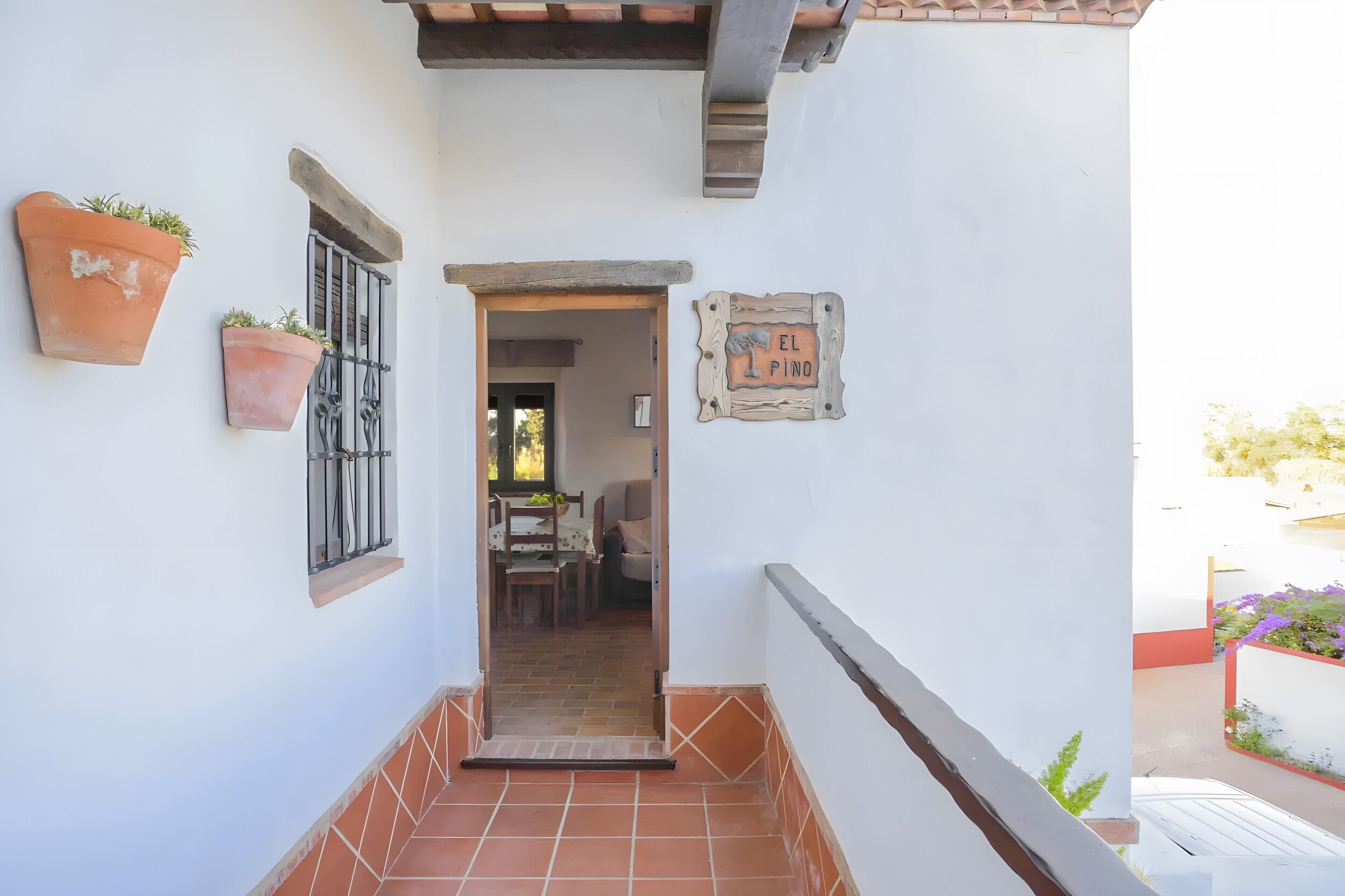 Un pasillo con baldosas de terracota, plantas en macetas, una puerta de madera y un cartel que dice 'EL PINO'.
