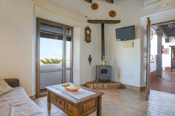 Una habitación con cama, una mesa, chimenea, televisor y ventana con persianas.