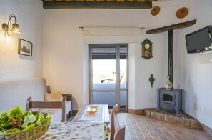 A cozy room with a sofa, a dining table with a floral tablecloth, a basket of fruit, a fireplace, and a television mounted on the wall.