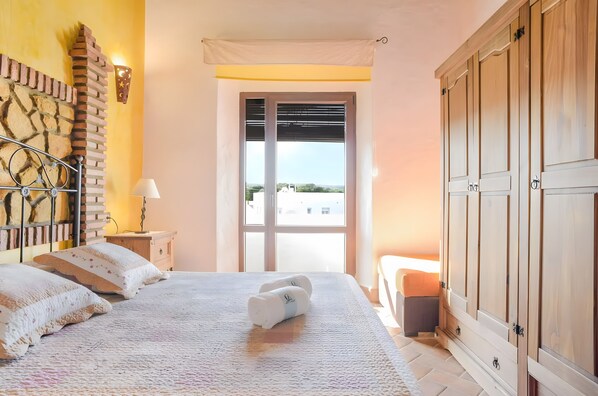 Une chambre à coucher comprenant un lit, une table de chevet, une lampe, une fenêtre avec des stores et une armoire.