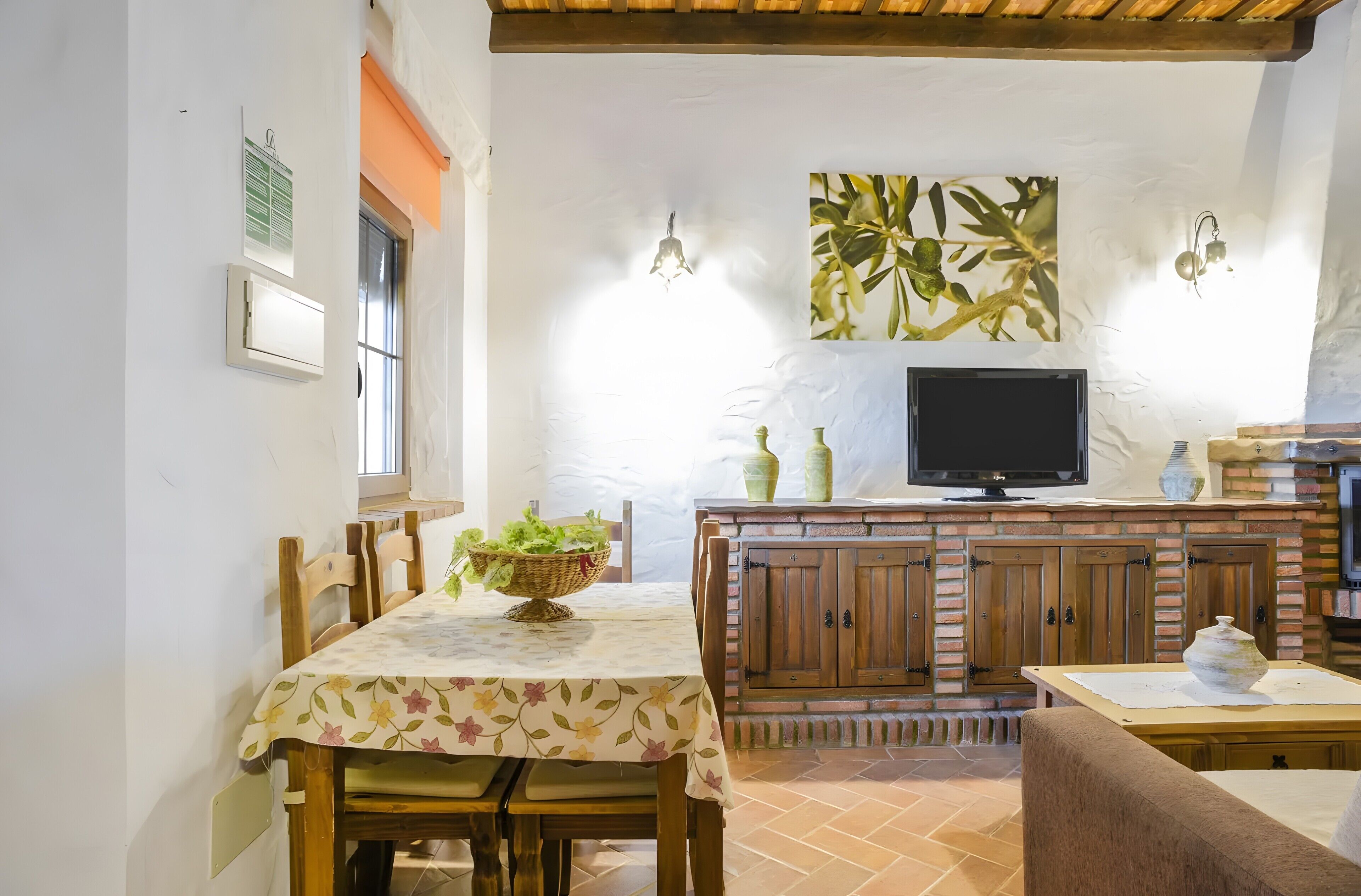 A dining area with a table set for two, a television, and a brick fireplace.