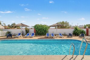 A swimming pool with clear blue water, surrounded by lounge chairs and a white wall.