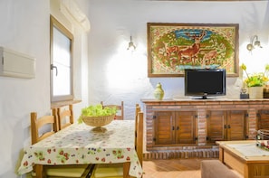 A dining area with a table set for two, a television, and a decorative painting above the TV. - Apartment 'El Nogal' with Shared Pool, Wi-Fi and Air Conditioning (Barbate)