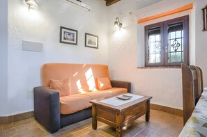 Un salon comprenant un canapé, une table basse en bois, une fenêtre ornée de grilles décoratives et des appliques murales.