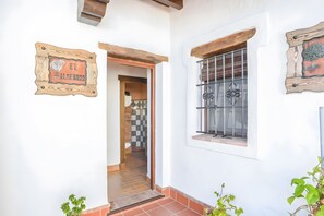 A house with a wooden sign reading 'EL ALMENORO,' a window with metal bars, and a door leading to an interior with a tiled floor. - Apartment 'El Almendro' with Shared Pool, Wi-Fi and Air Conditioning (Barbate)