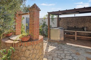 An outdoor kitchen area with a brick chimney, stone flooring, and potted plants.