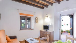 A room with a sofa, a small table, a TV on a wooden cabinet, and a window with a decorative grille. - Apartment 'Castaño' with Shared Pool, Wi-Fi and Air Conditioning (Barbate)
